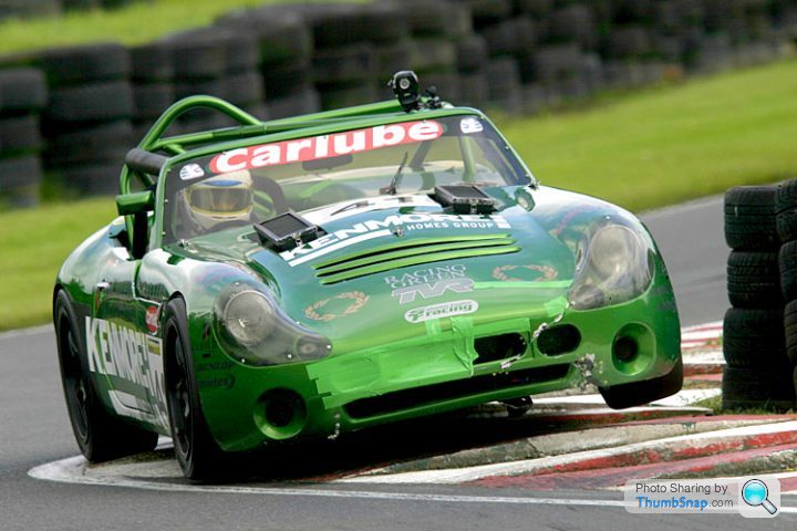 The annual what are you racing in 2014 thread.  - Page 1 - UK Club Motorsport - PistonHeads - The image captures a thrilling moment of a green car, displaying the name "Kenning", skillfully navigating the tight curve of a track. The vehicle is a sports car, equipped with a roll cage and a windshield, indicative of its readiness for high-speed racing. The tires are hooked to the road, demonstrating the driver's expert handling of the sports machine. The track, lined with hay bales for safety, forms a backdrop to this exhilarating scene, a natural setting for such adrenaline-fueled activities.