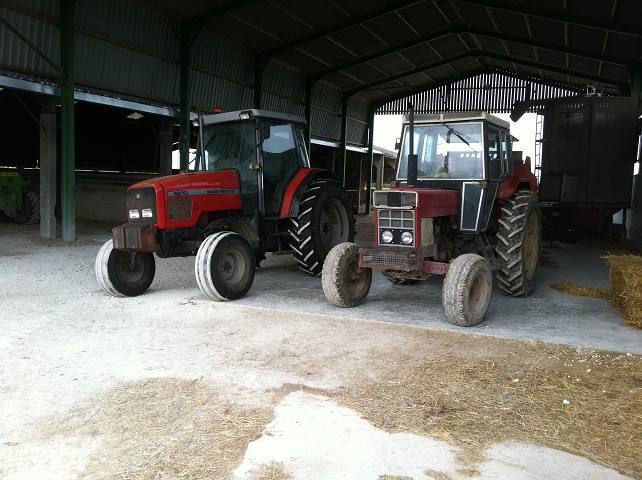 Classic tractors - Page 2 - Classic Cars and Yesterday's Heroes - PistonHeads - The image showcases a rural setting where two red tractors are parked inside what appears to be a barn. The tractors, equipped with large, fluffy tires, are positioned close to each other, taking up a significant portion of the space. The barn itself is large, with a high ceiling and wide doors. In the background, there's a glimpse of a stack of hay, indicating a traditional farm setting. The condition of the tractors and the hay suggest that this area is actively used for agricultural purposes.