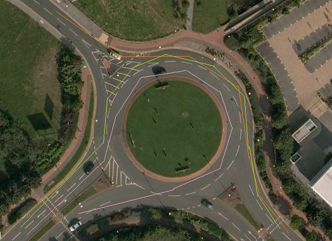 Roundabout Chevrons, - Page 1 - General Gassing - PistonHeads - The image presents an aerial view of a meticulously planned urban landscape. At the heart of the scene is a roundabout, elegantly manicured and a traffic island in the center perfectly maintained green lawn. Several vehicles are on the roads, following the marked green and yellow lines that are the road markings. The roundabout is surrounded by a grid of multi-lane roads, leading to various buildings and structures visible in the background. The overall layout showcases thoughtful urban planning with a priority on traffic management and aesthetically pleasing landscaping.