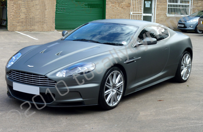 witch  black? - Page 1 - Aston Martin - PistonHeads - The image shows a silver Aston Martin Vanquish sports car on a paved surface. It's a daytime setting with the car positioned in front of the camera, allowing a clear view of its sleek design. The car's bodywork has a smooth, reflective surface, and it rides on large, alloy wheels. Behind the car, there is a building with a green door. The focus of the image is the car, and there's a watermark on the photo indicating it was taken in 2010.