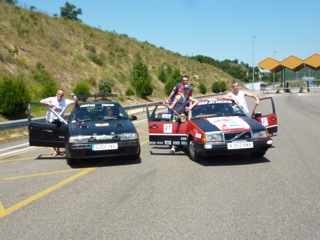 "Chip run cars win in Barcelona" - Page 1 - East Anglia - PistonHeads - The image depicts a group of people sitting in two sit-on car trailers at an intersection. The trailers are likely designed for motorbikes, with open platforms for vehicle racks. There are a total of six individuals visible; three in each trailer. All trailers have visible registration plates, indicating they are intended for on-road use. The surroundings suggest this might be a recreational or a team event involving motor traffic. The vehicles appear to be stationary, as the participants are relaxed and posing for the camera. There are no brand markings directly visible on the trailers.