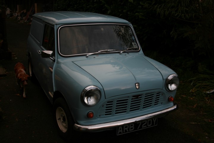 Lets see a picture of your classic(s) - Page 134 - Classic Cars and Yesterday's Heroes - PistonHeads - The image captures a charming scene of a vintage, light blue Volkswagen Beetle car sitting on a driveway. The car appears well-maintained, with a rectangular window framing its compact form. A curious brown dog stands attentively beside the vehicle, adding a touch of life to the scene. Behind the car, a lush, tree-filled yard extends, creating a serene backdrop. The overall atmosphere of the image is peaceful and nostalgic.