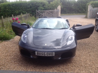 Ferrari F430 F1 Spider....finally about to take the plunge.. - Page 1 - Supercar General - PistonHeads - The image shows a black sports car parked on a gravel driveway or area paved with gravel, with its doors wide open. The rear doors of the car are likely intended for easy ingress and egress to the cockpit. From the perspective of the image, it appears as if the car is newly parked or has just come to a halt. Additionally, there is a plate or tag visible, although the text on the tag is not legible. The sun is out, shining on the side of the car. The setting seems to be a rural or semi-rural location, as suggested by the gate in the background.