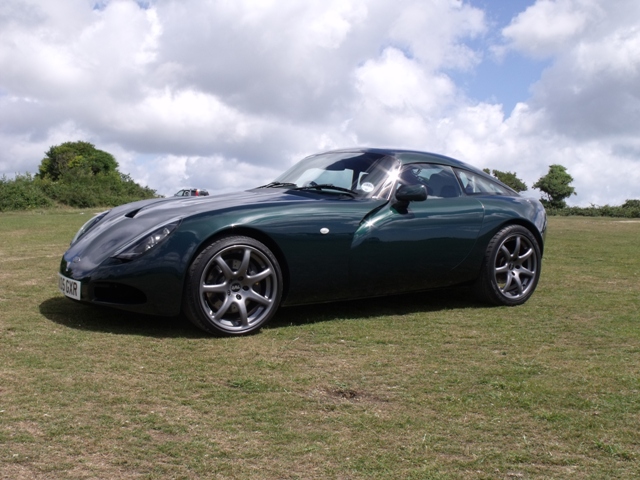 New T350 owner saying Hi. - Page 1 - Tamora, T350 & Sagaris - PistonHeads - This image captures a silver sports car parked in a grassy field. The car has a sleek and aerodynamic design with distinct wheel arch molding and alloy wheels. It is positioned at an angle to the viewer, showing a side profile view. The background is adorned with a sky filled with clouds, contributing to the picture's overall tranquil and open space ambiance. The image exudes a sense of elegance, speed, and style associated with the car's image. The perspective and framing of the shot highlight the car's elegance and design.