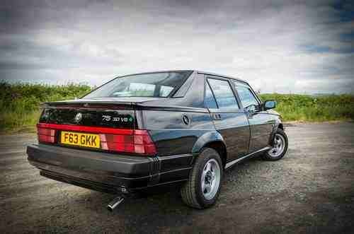 A black and white photo of a car parked in a field - Pistonheads - The image depicts a dark blue coupe parked on a gravel road. The car features distinctive vertical taillights that add to its sleek design. The setting includes an open sky filled with clouds, which provides a dramatic backdrop to the car. Off to the side, greenery can be seen, suggesting a rural or semi-rural location. There are no visible texts or branding on the car that can be confidently identified.