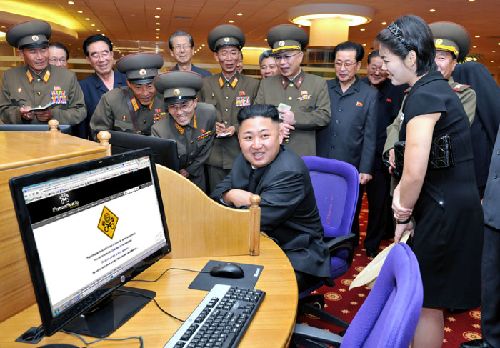 North Korea photoshop contest - Page 9 - The Lounge - PistonHeads - The image is a photograph depicting several people in a group setting. At the center of the frame, there is a man sitting attentively in front of a computer monitor that displays a website. To his left, there is a desk with a keyboard and mouse, next to a purple office chair. The surrounding individuals include others in office attire, suggesting a formal or professional environment. The atmosphere appears to be serious, and the location may be an intergovernmental meeting or a business gathering.