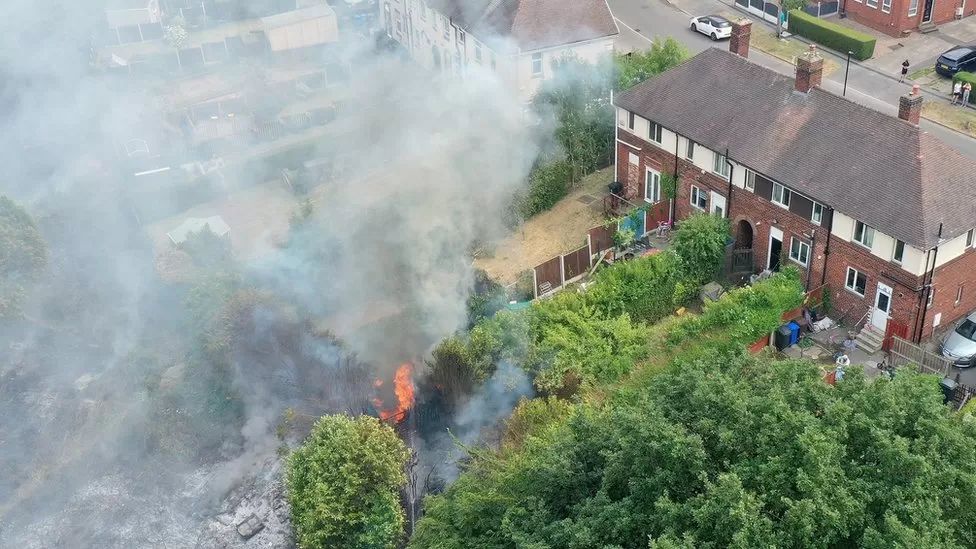 Pistonheads - The image shows a scene of a fire. There is a large plume of smoke rising into the air, indicating an intense blaze. Below the smoke, there's visible damage, suggesting that the fire has been burning for some time or is quite significant in size. On the ground, you can see what appears to be burnt rubble and debris, likely the remnants of a building that has been severely damaged by the fire. The background reveals that this incident has occurred on an urban street corner, with houses and buildings visible nearby. There's no sign of any people or animals in the immediate vicinity of the fire, suggesting that the area might be cordoned off for safety reasons.