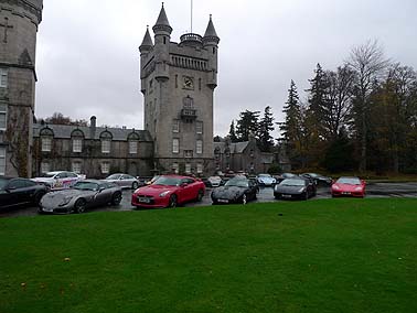 Pistonheads - The image captures a serene setting in a parking lot, where several cars of various colors are neatly parked. The dominant feature in the background is a majestic castle-like structure with a tall tower piercing the cloudy sky. The grassy field in front of the cars and the castle provides a soft contrast to the urban elements. The overall scene presents an interesting blend of nature and architecture.