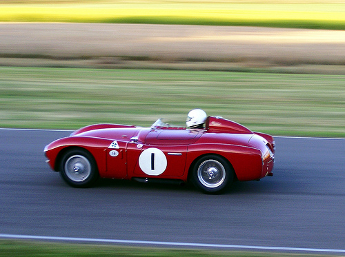 A red and white car with a red bow on it - Pistonheads - This image captures a moment of speed and precision on a race track. At the center of the frame is a vintage race car, painted in the classic red and white livery that evokes the glory days of motor racing. The car is adorned with the number 1, indicating its position in a race or its status as a premier vehicle in the sport. The driver, clad in a helmet and racing suit, is in control, skillfully maneuvering the car around a sharp turn on the track. The background, a blur of green and brown, suggests the track is set in a countryside setting.