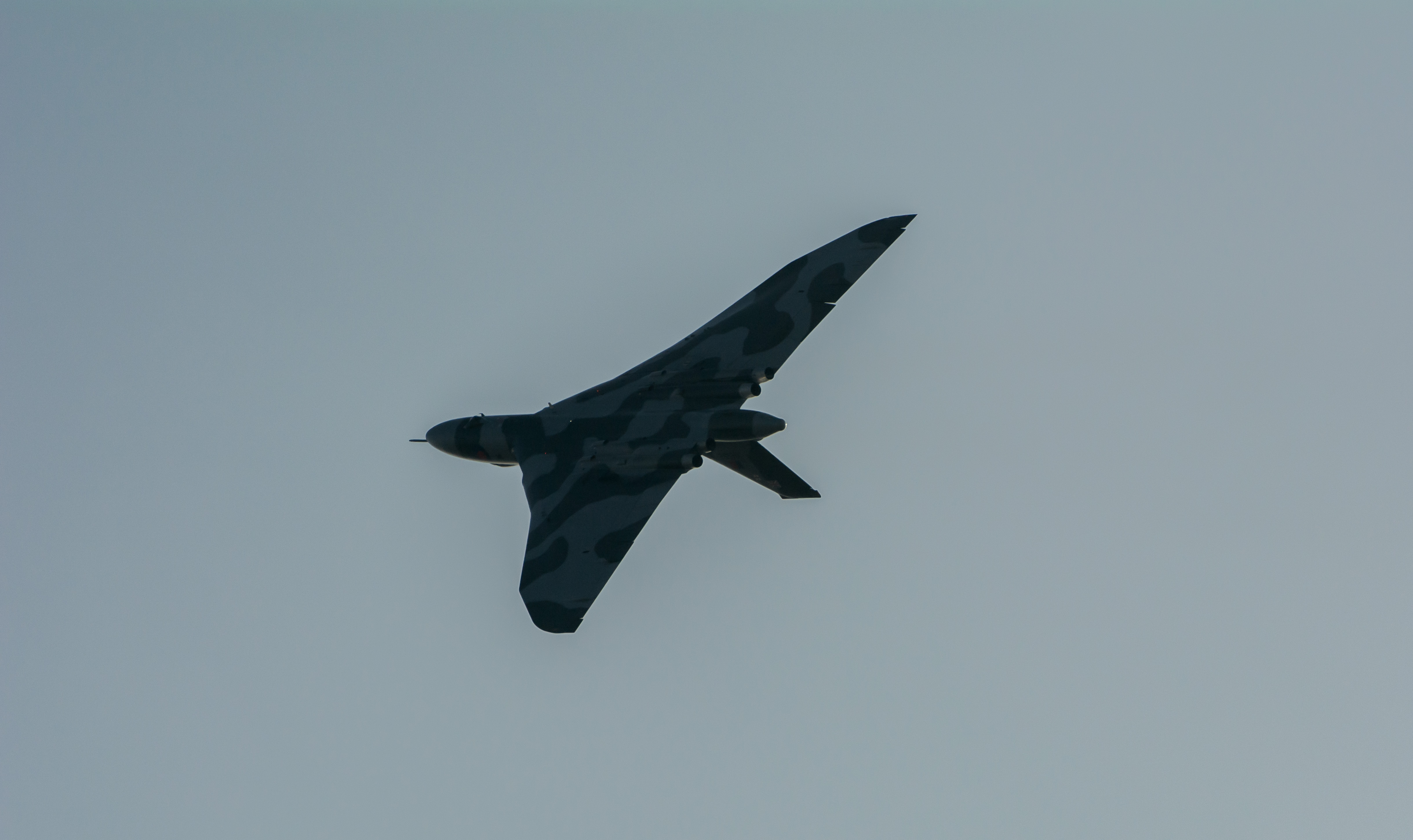 An airplane flying through a blue sky with a propeller - Pistonheads - This image captures a solitary military aircraft in flight. The aircraft, displaying a camouflage pattern, is angled slightly away from the viewer, with its nose pointing upwards. Its position in the sky against a backdrop of grey hues suggests the photo was taken on an overcast or cloudy day. The aircraft is not projected favorably, indicating the photo may have been rotated incorrectly. There are no additional elements or objects visible in the image, indicating the aircraft is the main subject.