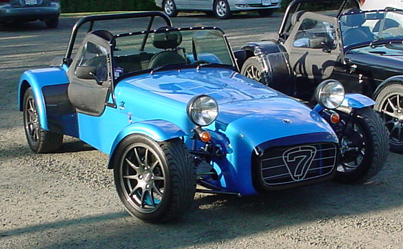 Kingfisher Blue Caterham Viper Pistonheads - The image showcases a trio of one-off car designs, each distinct in color and features. Leading the trio is a striking blue car with an open top, giving it a unique feel. 

The second car is draped in black, adding a dramatic touch to its appearance. The third car, positioned towards the right side of the image, is black and sporty, with a similar open top design as the blue car. 

The cars are parked on a gravel surface, suggesting an outdoor or rural setting. The unique designs and vibrant colors of the cars make for a visually appealing scene.