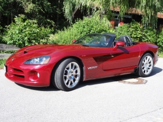 Years Pistonheads Celebrating - This image shows a vibrant red Corvette convertible parked on a concrete surface. The car's top is down, revealing its sleek interior. The background is filled with lush greenery, suggesting that the setting might be a garden or a park-like area. The Corvette is the main focus of the image, taking up a significant portion of the scene. There are no people or other objects present in the scene.