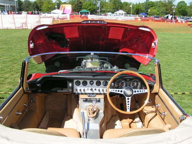 1961 E Type - Page 1 - Readers' Cars - PistonHeads - The image displays the interior of a classic, possibly vintage car, focusing on the open trunk. The car's interior is rich in texture, featuring a clean tan interior and chrome details. There are control knobs visible, suggesting the presence of a retro-type sound system, which is consistent with the car's overall design. The photo is taken in natural light, indicating that the vehicle is parked outdoors. The vehicle's trunk is open, revealing the storage compartment. It appears to be well-maintained, with no visible damage or wear. The car's colors, red, black, and tan, contribute to a sense of nostalgia and luxury.