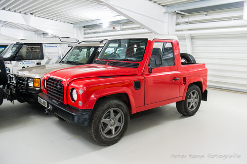 RE: Defender makes UK debut at Goodwood Revival... - Page 3 - General Gassing - PistonHeads - The image shows a small red car parked indoors. It appears to be an off-road vehicle, with rugged design elements such as raised ground clearance and large wheels. There are no visible license plates on the car. In the background, there is a truck that seems to be part of the same indoor setting. The style of the image suggests it might have been taken for a catalog or inventory purpose, given the clean and even lighting.