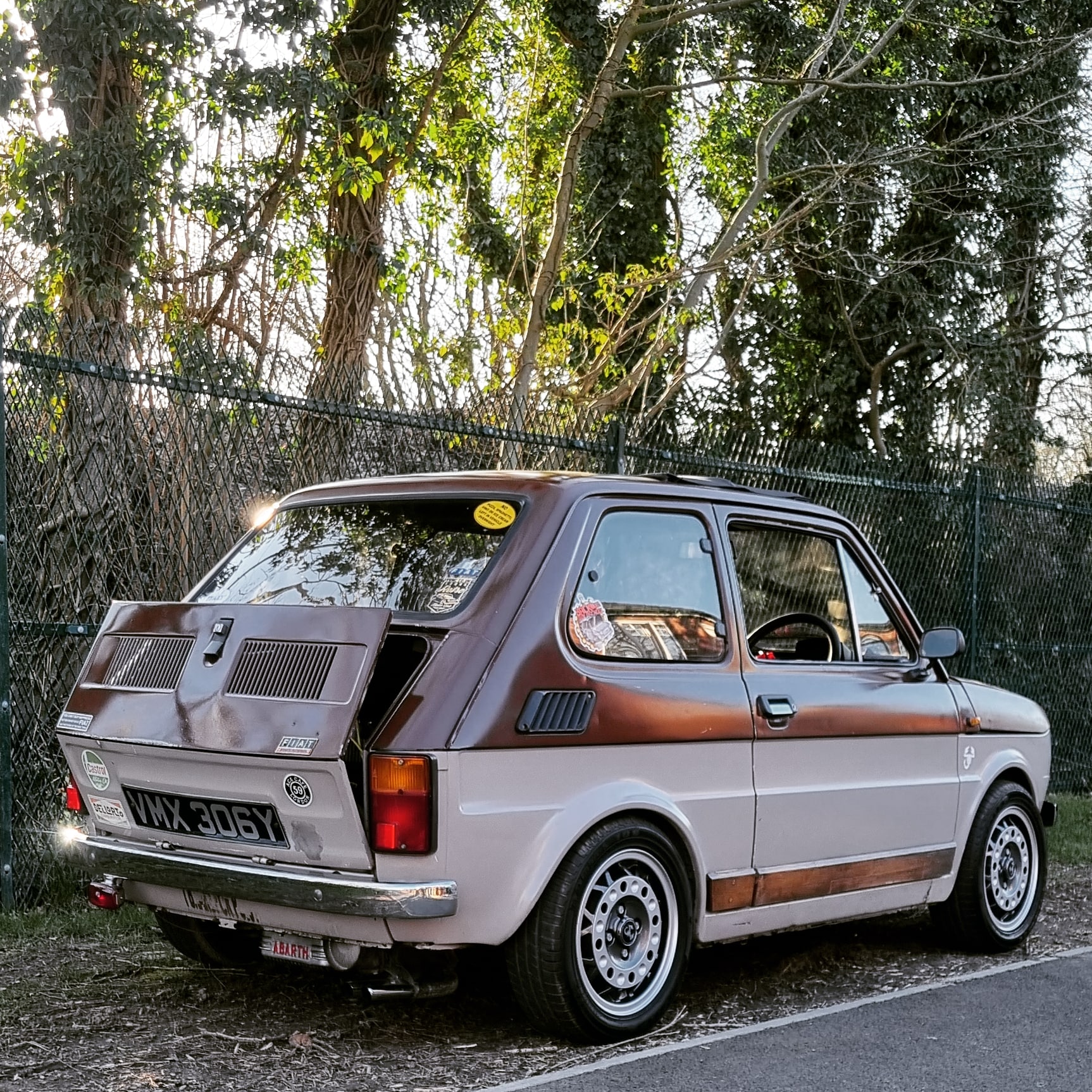 1982 Fiat 126 - Page 4 - Readers' Cars - PistonHeads UK - The image features a vintage car parked on the side of a road. The car is a striking combination of brown and white, reminiscent of an era gone by. It's parked near a fence, under the watchful eye of trees in the background. A building with a red roof can be seen behind the car, adding to the overall rustic charm of the scene. This image captures a moment frozen in time, evoking a sense of nostalgia and the enduring appeal of classic vehicles.