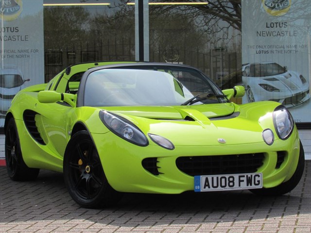 Krypton Green Elise - Page 1 - Elise/Exige/Europa/340R - PistonHeads - The image features a striking lime green Lotus car, prominently parked in front of a dealership. Its sleek design is accentuated by the vibrant color and the presence of the Lotus logo on the front of the vehicle. In the background, there's a large window reflecting the car, and a signboard advertising a car show. The attention to detail and the shiny exterior of the car suggest it might be new or well-maintained.