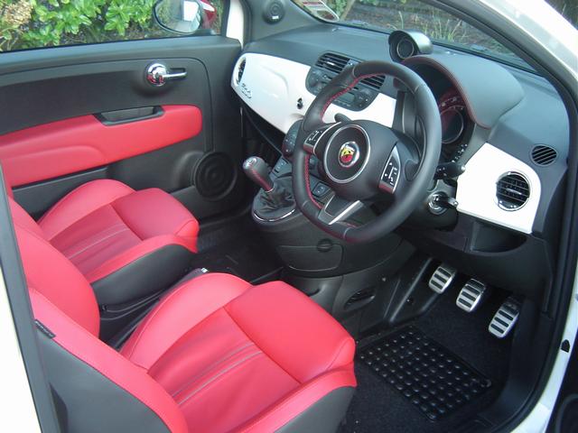 Cars with a body coloured dash - Page 1 - General Gassing - PistonHeads - The image displays the interior of a car, focusing on the front seats and center console area. The seats are predominantly red with black padding, and there's a steering wheel with a circular emblem, suggesting it's a luxury or high-end vehicle. The center console features what appears to be multiple power plates or charging stations for different electronics, set into a panel with enough space for additional storage. The door panel is also visible, showing the handles and mirrors, which are in a matching red and black design. The overall atmosphere of the car is sleek and modern, with a luxurious feel conveyed by the high-quality interior.