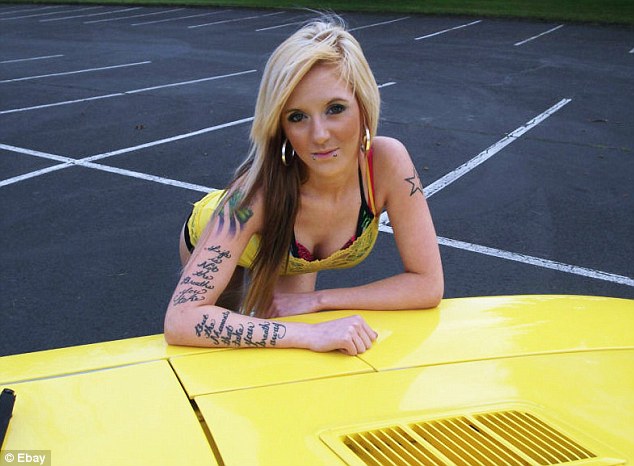 Bad Tats - Page 39 - The Lounge - PistonHeads - In the image, a woman with long blonde hair and tattoos on her arms is sitting on the hood of a bright yellow car. She has a casual yet striking outfit consisting of a colorful bikini top. Her pose is relaxed against the car, and she is looking directly into the camera. The car is parked on an asphalt surface with white parking lines, and there is a single star visible in her tattoo collection. The setting appears to be an empty parking lot.