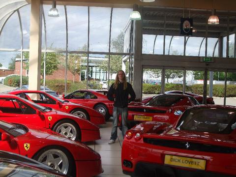 Jason Met Pistonheads Plato - In the image, an individual stands amidst a stunning collection of red Ferrari cars, gathered in a showroom. The showroom itself is a spacious room with a high ceiling, characterized by a large glass wall that provides a clear view of the vehicles outside. The Ferraris outside vary slightly in model, but all exhibit the iconic design and branding that the marque is known for. The overall scene suggests an event or display of Ferrari's finest, with the showroom functioning as an attractive destination.