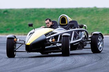 atom or noble ? - Page 1 - Ariel - PistonHeads - This image depicts a man in a yellow and black single-seater racing car on a curved track. The racer appears to be moving at high speed, as suggested by the rear tire's sideways position indicating a quick turn. The background is slightly blurred, providing a sense of motion and speed. The setting implies a racing event, possibly an automobile or possibly a motorcycle race due to the design of the vehicle.