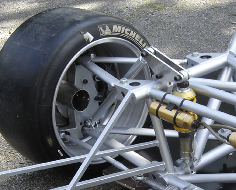 Full Max Underbody Downforce Tray Pistonheads Thought - The image focuses on the bottom of a car, showing a view of a Michelin tire attached to a gray wheel. The tire is black and appears to be well-worn. A metal suspension system with Yellow joints is visible, supporting the weight of the vehicle while maintaining control over the suspension. This suggests that the vehicle is possibly a race car or a car with specialized suspension requirements. The image is taken from a low angle, looking up at the underside of the car, emphasizing its mechanical structure.