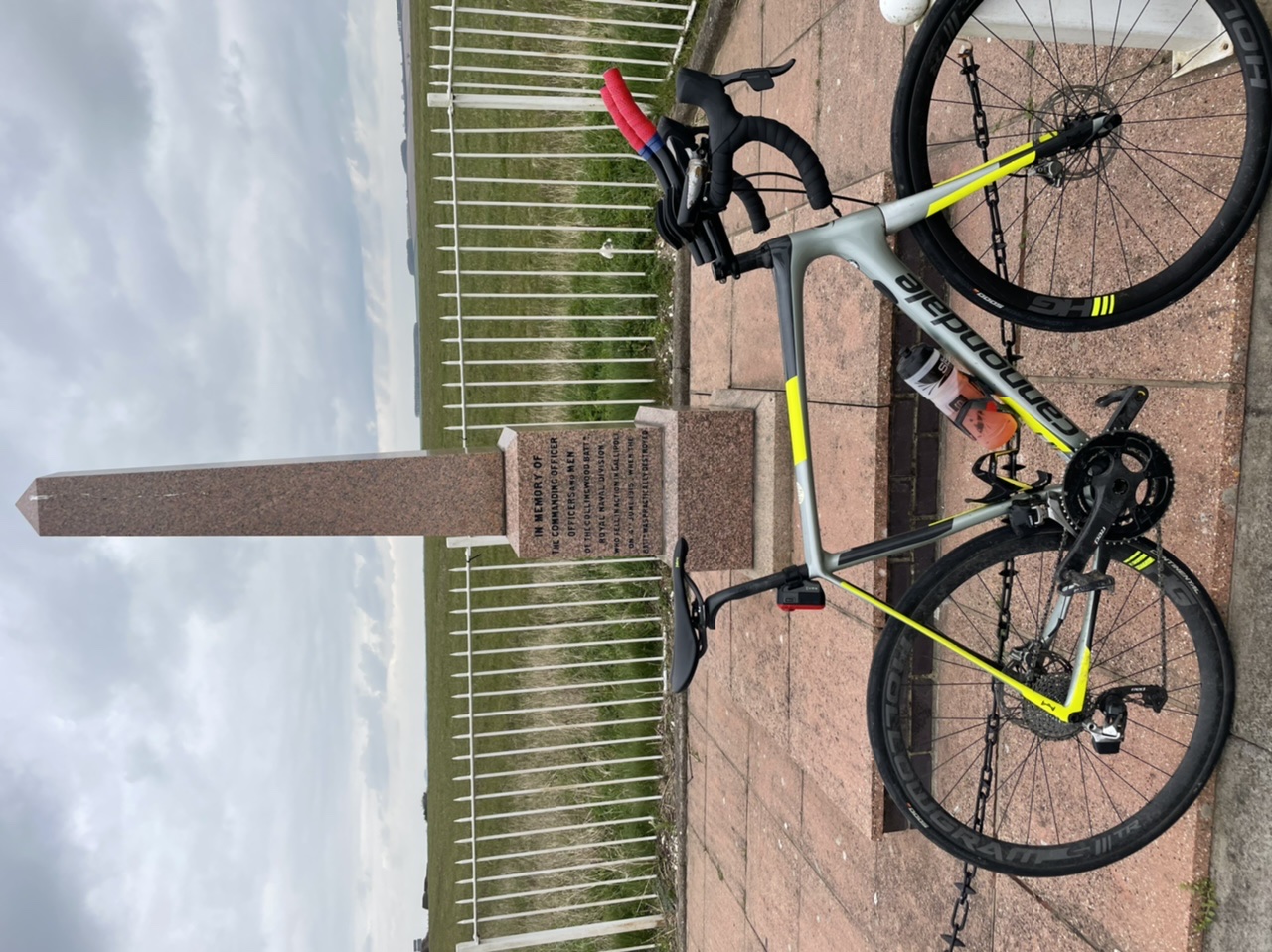 The "Photos From Today's Ride" thread. (Vol. 2) - Page 3 - Pedal Powered - PistonHeads UK - This image shows a bicycle parked next to a small plaque on a concrete base. The bike has a prominent yellow and black color scheme, suggesting it's a mountain bike designed for rough terrain. There are various components visible, including the frame, wheels, and handlebars. The handlebars also have several cables and accessories attached, which is typical for off-road bikes. The background features a simple stone wall, indicating that this scene takes place in an outdoor setting, possibly a park or cycling path. There are no people visible in the image.