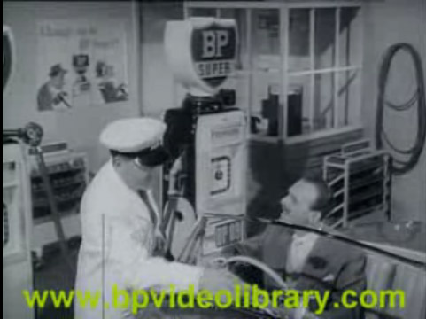 Identity Alfa Pistonheads Required - The image appears to be an archival still from a 1960s film showing an indoor scene of a vintage clothing store. Two males are visible, engaged in a conversation; one is dressed in a white uniform and cap, possibly a shop employee, while the other is in casual attire. In the background, vintage sewing machines and mannequins are displayed, indicating an emphasis on tailoring and fashion. The setting suggests a realistic depiction of a historical store. The image also has a watermark, website link, and file name overlaying it.