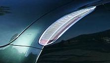 A blue car is parked on the beach - The image is a close-up photograph focusing on the bright light of a car's left rear tail light. The tail light is reflected in the glossy surface of the car's body, creating an interaction that highlights the vehicle's design. The light casts a white glow slightly above the black color of the car, which is visible in the reflection of the tail light. The dark background accentuates the brightness of the vehicle's light, contributing to ahigh-contrast image.