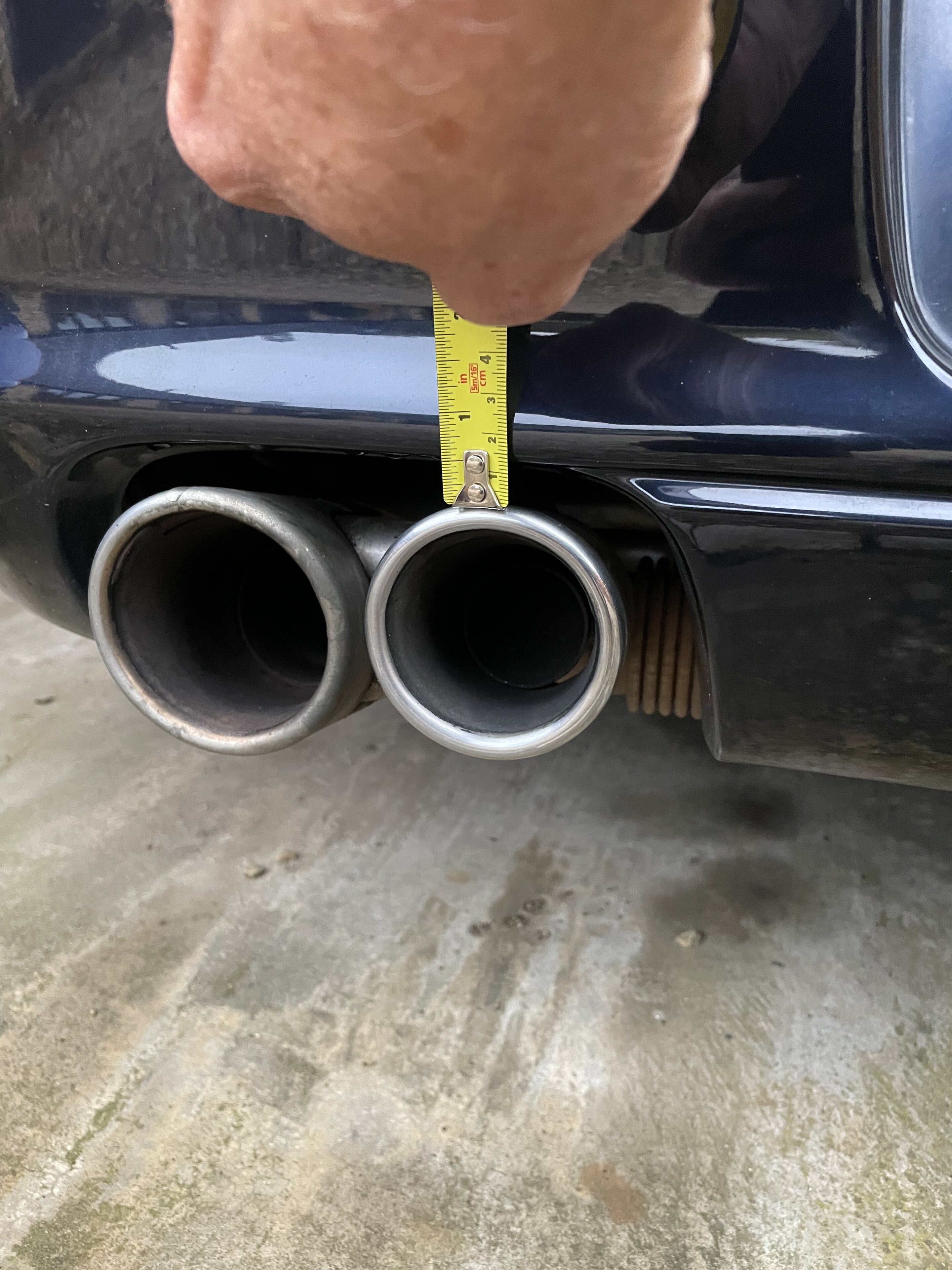 Pistonheads - The image shows a car with its exhaust pipes exposed, indicating it may be an older model or modified to expose the piping. A person's hand is visible in the bottom right corner of the photo, holding a measuring tape against one of the pipe holes. This suggests that someone might be checking the size or condition of these pipes. The car appears to have two exhaust pipes, both prominently featured in the image. There are no texts or distinctive brands visible in the image. The background is indistinct and does not provide additional context about the location or event.