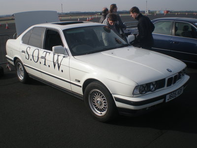 Helga Bmw Pistonheads - The image showcases a white BMW 530i car parked on a tarmac lot. The car is adorned with a distinctive "S.O.T.W" script on its doors. Two people are standing near the back of the car, engaged in conversation. In the immediate background, there are other cars parked, hinting at a larger area or event. The scene suggests an outdoor gathering or event, possibly a car show or a group meet-up.