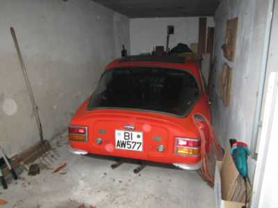 Early TVR Pictures - Page 35 - Classics - PistonHeads - The image depicts an orange car parked in a garage with a concrete floor. The car has a visible license plate that reads "BI A767". To the left of the car, there's a broom leaning up against a wall, and in the corner, to the right, there's a small blue object, possibly a bag or a container. The overall impression is of a typical residential garage storage.