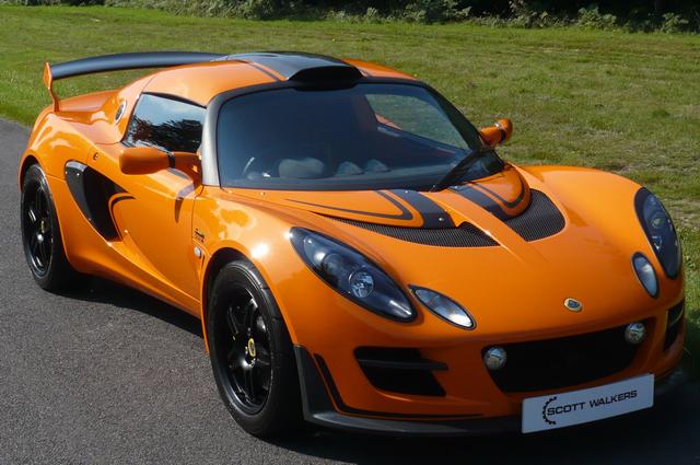 Pistonheads - The image captures a sleek, orange sports car parked on a roadside, exhibiting a low, snubbed front profile that suggests high-performance capabilities. The vehicle's design elements, including the aerodynamic front bumper and the wide air vents on the hood, highlight its sporty nature. The car features black contrast details on the vents and a rear window window wiper, matching the alloy wheels. The license plate reads "SCOTT WANDERS," indicating the car's identification in public.