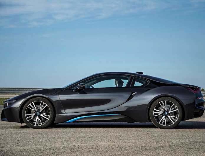 BMW i8 - Page 1 - Aston Martin - PistonHeads - The image features a sleek, black sports car with intricate details, such as stylish rims, visible on its tires. It's parked on a road, with the vast expanse of the open sky serving as a stark contrast to the car's polished exterior. The car's design and the blue sky give the picture a dynamic yet serene feel. The surroundings appear to be relatively unoccupied, allowing the sports car to command attention in the frame.