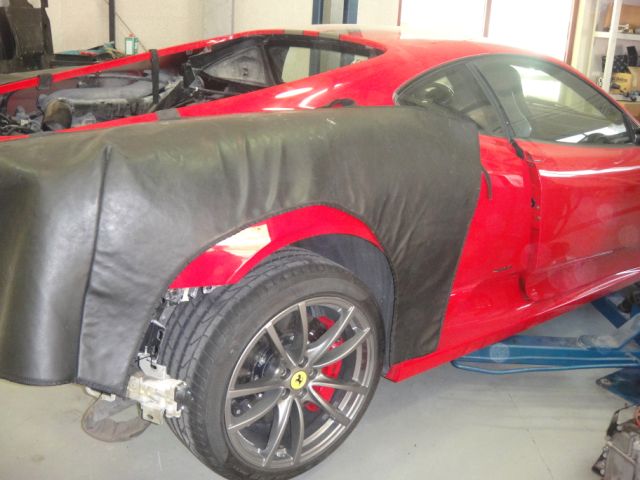 My First Ferrari...and its a Scud! - Page 1 - Ferrari V8 - PistonHeads - The image depicts a sports car in a garage, having partially clear coverings that reveal a red body and black interior. The vehicle is positioned in front of a cabinet on the left side of the image. The coverings bear remnants of a yellow and black striped theme, indicating a previous modification or branding. The car's design is sleek and aerodynamic, with features like a large spoiler and intake vents, suggesting a performance orientation.