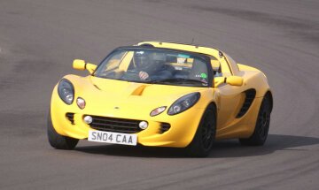 135r - Page 1 - Elise/Exige/Europa/340R - PistonHeads - The image captures a dynamic scene of a yellow sports car in motion on a race track. The license plate of the car reads "SNO4 CAA", indicating it's registered and on the road. The car's bright yellow color stands out against the track, suggesting speed and performance. The setting is an outdoor race track, identifiable by its curving lanes and dry, paved surface. The image does not contain any people or significant action in sight.