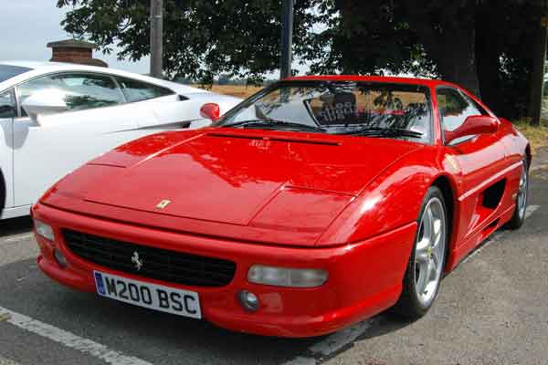 A red car is parked in a parking lot - Pistonheads - The image depicts a striking scene on a roadway. Dominating the view is a vibrant red sports car, its glossy finish hinting at its speed and power. It's parked on the right side of the road, adjacent to a sleek white sports car, their contrast bordering on dramatic. The lush green trees in the background add a touch of nature to the urban setting. Despite the mention of a white car, there's no textual confirmation within the image itself to back this up.