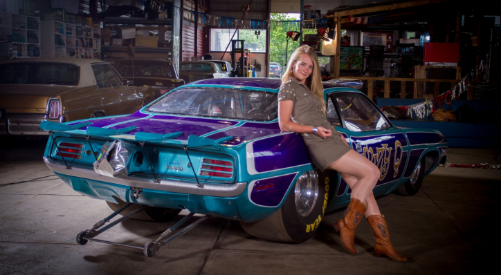 Fastest ladies always drive Mopars lol - Page 1 - Drag Racing - PistonHeads UK - The image shows a woman posing with a customized, colorful classic muscle car in what appears to be a workshop or garage setting. She's dressed casually and is sitting on the front fender of the car, leaning against it. The vehicle has a vibrant paint job with various designs and patterns. In the background, there are shelves filled with items that suggest a mechanical or automotive environment. The car features prominent modifications such as a large rear wing and a custom hood.