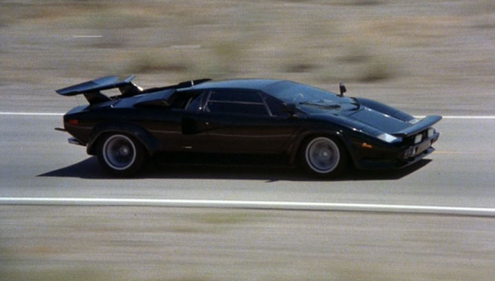 A Pic of The Car That First Turned You Into A Petrolhead? - Page 7 - General Gassing - PistonHeads - This image presents an exhilarating scene on a road. As the focal point of the image, a black sports car is captured in mid-motion, racing rapidly in the right lane of a highway. The car's sleek design, combined with its distinct spoilers on the hood and the two on the back wing, emphasizes its racing capabilities. The road itself is largely clear, creating an unobstructed view of the car's fast-paced journey. The speed of the car is possibly suggested by the blurring effect around it, which suggests movement and adds a sense of motion and dynamism to the image.