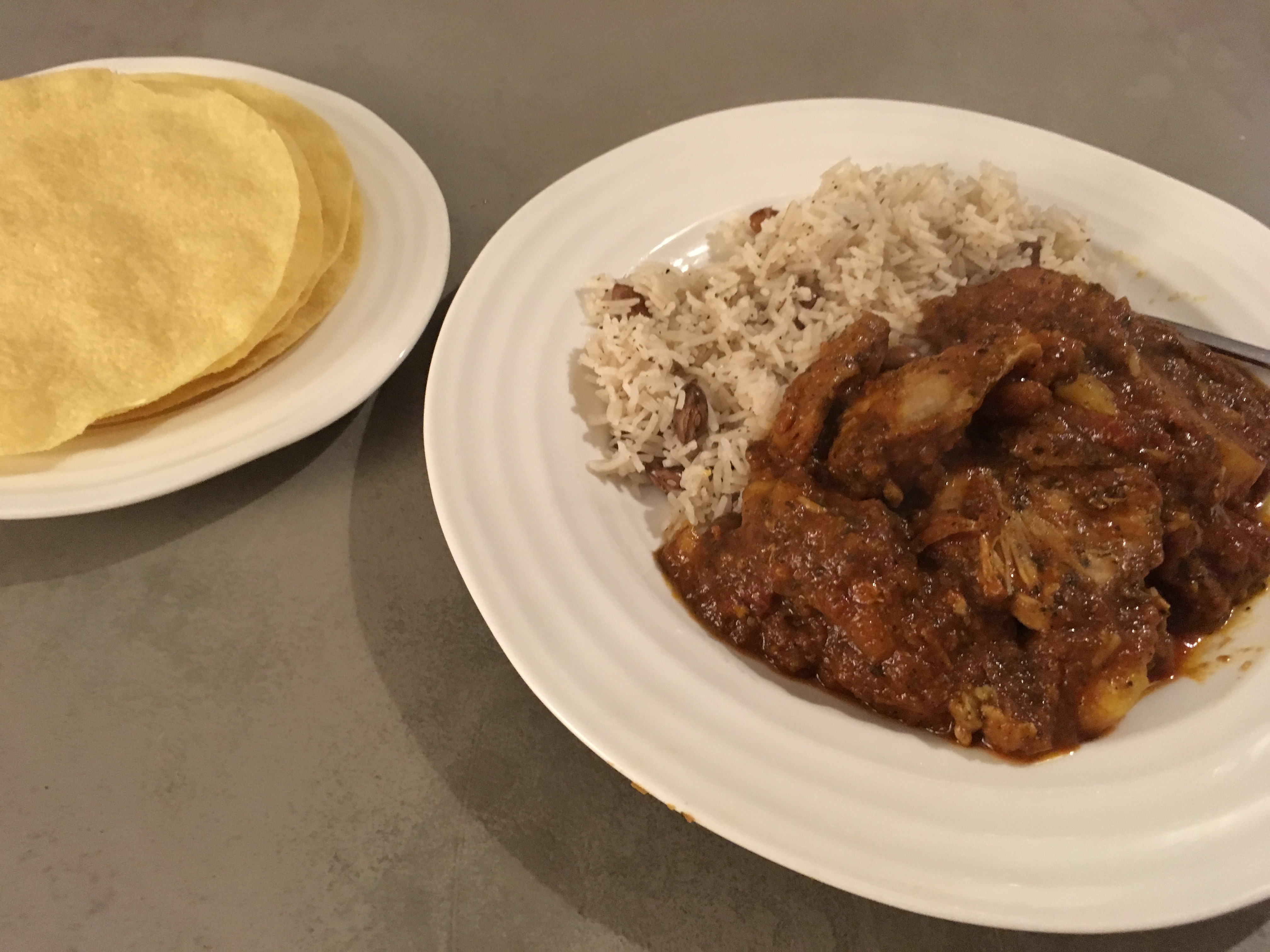 PH Cooking Competition - Curry - Page 1 - Food, Drink & Restaurants - PistonHeads - The image presents a tasty-looking Indian meal served on a dining table. At the center, there is a white plate filled with a warm, rich curry, next to a portion of steaming white rice. A stack of round flatbreads, or papadums, is situated on the left side of the plate. A spoon is hinted at, suggesting the meal is ready to be enjoyed. The overall setting creates an inviting and appetizing atmosphere.