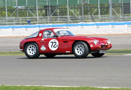 Early TVR Pictures - Page 32 - Classics - PistonHeads - In the image, a vintage red race car labeled with the number 72 is prominently featured. The car, emitting a sense of speed and performance, is positioned on a track. Its design, doors wide open, suggests a driver's car. The background reveals a stretch of gray track with barriers, indicating a racing environment. This scene is set in a clearing where the main focus is the impatient race car and its surrounding environment.