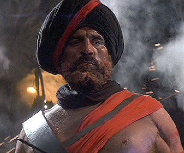 A man wearing a hat and a hat - Pistonheads - The image portrays a middle-aged man with a stern expression. He is wearing traditional Middle Eastern attire, including a black turban and a black and red robe. The turban is accentuated with a red and black headband. The man appears to be indoors, with lights and smoke in the background, which gives the image a dramatic and intense atmosphere. There is no visible text on the image. The focus of the image is on the man and his distinctive attire.