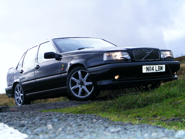 Newby Pistonheads Introducing - The image portrays a dark-colored sport sedan carving a path through a grassy area. The vehicle is resting atop a patch of grass and gravel, perhaps parked or slowly moving through the terrain. The background features a sky filled with clouds, adding a dramatic effect to the image of the stationary car. The license plate on the car is clearly visible, reading " N14 LWR." The car's design and the surrounding natural environment create a contrast between the man-made and the natural elements.