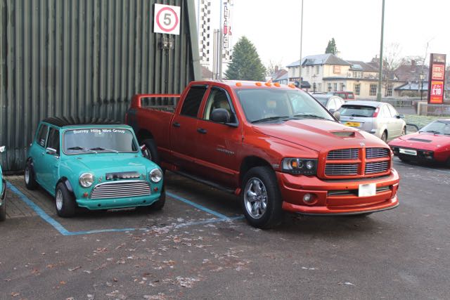 A red truck parked on the side of a road - Pistonheads - This image captures a scene in a parking lot where two small-sized vehicles, one blue and the other red, are parked side-by-side. They are small in size, and their vibrant colors stand out against the backdrop of the parking lot. To the right of these cars, there is a larger vehicle, a red RAM pickup truck, which is parked at a slightly different angle to the small cars. In the distance, a few more cars can be seen, parked in their respective spots. On the left side of the image, there is a sign adorned with the number 5, providing a bit of context for the location. The overall scene suggests a public parking area, possibly indicating a popular spot or perhaps highlighting a quiet time of day. The precise arrangement of these vehicles and the sign in the distance creates a sense of order amidst the everyday hustle and bustle.