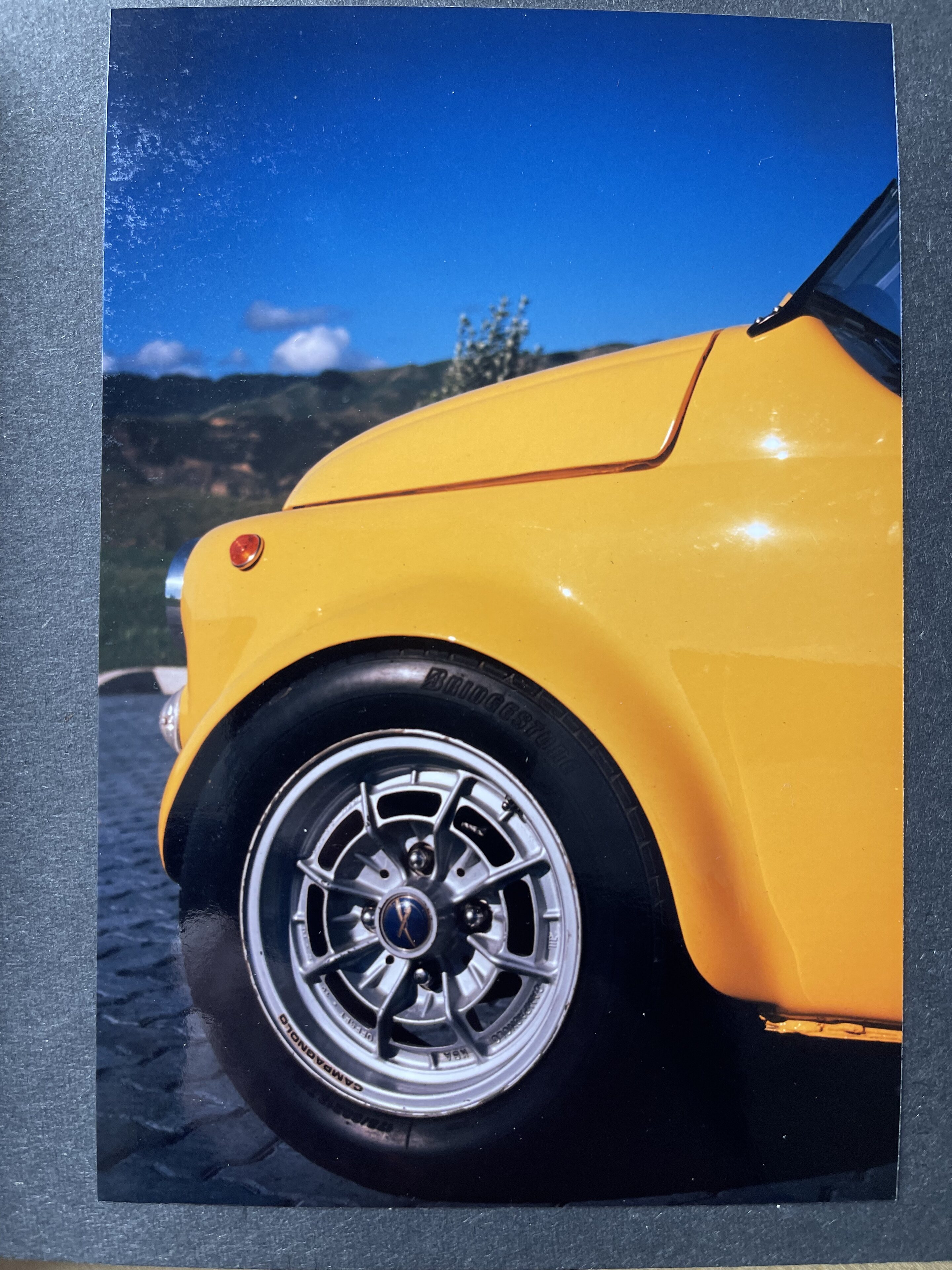 A red car is parked in a parking lot - Pistonheads - The image shows a small, square format photo of a vintage car. The car is predominantly yellow and is parked in what appears to be an open outdoor space, possibly a parking lot or a driveway. It features unique design elements such as chrome accents, custom wheels, and a distinctive shape that suggests it might be from the 1960s or 1970s. The background of the photo is out of focus but hints at a clear sky, suggesting that the photo was taken during the daytime under good weather conditions. There are no visible texts or distinguishing marks on the car or in the image that would provide additional context about the location or the nature of the event captured in the photograph. The image itself has a straightforward composition, with the car occupying most of the frame, and it is the main subject of the photo.