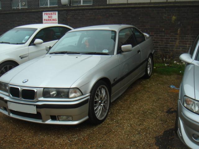 Pistonheads - The image showcases a sunny day with several cars parked on a gravel surface. A silver BMW coupe is prominently featured in the foreground, exuding a sleek, four-door design. Other cars, including a white sedan and a silver SUV, are also present in the background, sharing the same parking area. The cars seem to be parked near a brick building, which is partially obscured with a "private parking" sign. The scene evokes a sense of tranquility and orderliness.