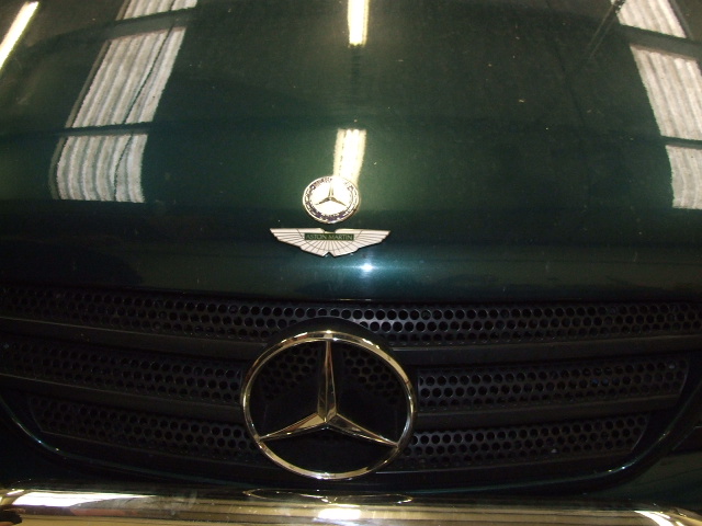 Light Pistonheads Shed - The image is a close-up photograph featuring the grille of a luxury vehicle. The car's front grille has a sleek, metallic finish with numerous small holes or ventilation slots arranged in a pattern. In the center, there is a prominent Mercedes-Benz logo, which is a round badge with an airplane silhouette and the brand name within the circle. The reflection of the window blinds can be seen over the hood of the car, and the vehicle appears to be well-maintained with a shiny exterior. The setting suggests an indoor environment, likely a car dealership or a service center, as indicated by the artificial reflection and the quality of lighting.