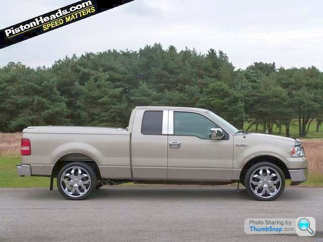 Pistonheads - The image features a beige full-sized pickup truck parked on a road with a natural backdrop. The truck is equipped with a bed liner and includes a crew cab configuration with a four-door cab and a five-passenger capacity. The vehicle has six wheels visible in the frame, indicating it may be an off-road or four-wheel-drive model designed for additional versatility. The setting suggests a rural or suburban area with greenery and trees in the background.