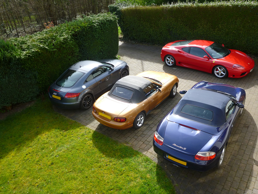 Keep or sell our one-owner Mk2 dilemma? - Page 1 - Mazda MX5/Eunos/Miata - PistonHeads - The image shows a serene outdoor setting where four luxury sports cars are parked in a circular formation on a cobblestone driveway. The colored sports cars feature a mix of gray, blue, and red, each displaying an elegant design. They are positioned in front of well-maintained, manicured hedges and lawns, creating a picturesque setting.