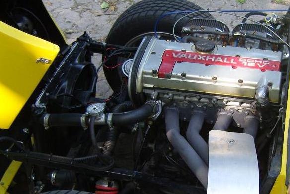 Pistonheads Cooling System - The image shows a vintage car engine. A large and central Vauxhall 90EX V12 engine is prominently displayed in the photograph. There are black pipes diagonally running on either side, indicating a complex and dense engine layout. A prominent label "Vauxhall" is visible, suggesting the make of the car. There are also visible hoses and tubes that connect different parts of the engine. The background is softly focused, focusing attention on the engine.