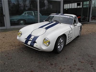 Early TVR Pictures - Page 55 - Classics - PistonHeads - The image shows an older model white sports car with a distinctive body striped in blue and white stripes on the hood. The car is parked on a paved lot, which can be seen through the vehicle's clear windshield. The setting suggests it might be outside a building, with the car facing towards the left side of the frame. There are no visible texts or distinctive brands that can be confidently identified in the image. The style of the car indicates it could be a classic or vintage model.